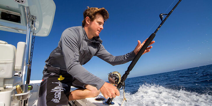 Young man grabbing trolling rod at stern of boat