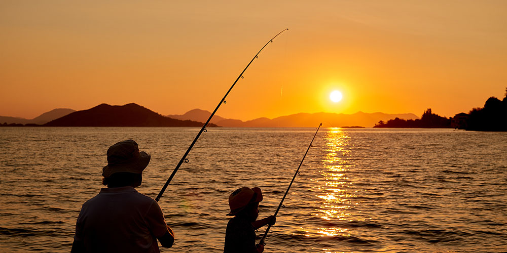 Father and young son fishing from pier at sunset