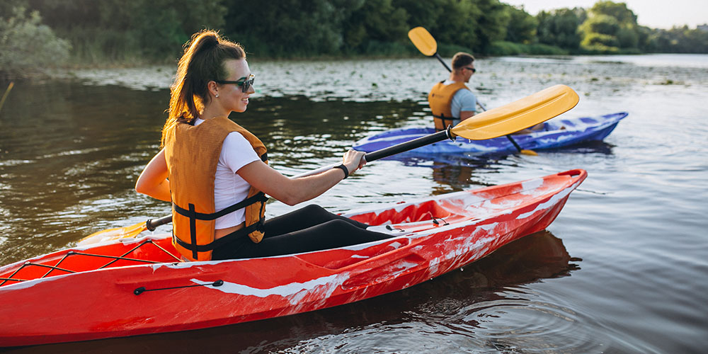 A man and a woman wearing life jackets paddling their kayaks on a river