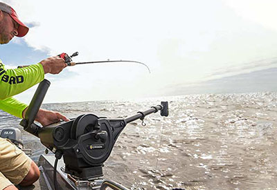 Angler with fishing rod standing next to downrigger in use