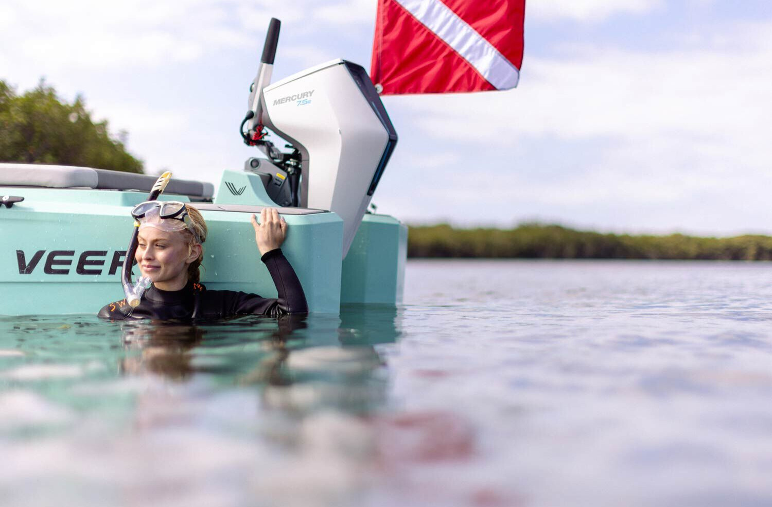 person in the water next to a boat with a Mercury electric outboard attached