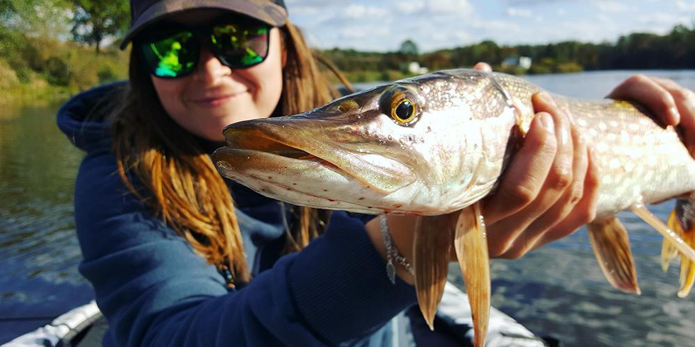 Woman in kayak holding large pike up to camera