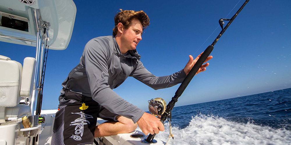 Young man grabbing trolling rod at stern of boat