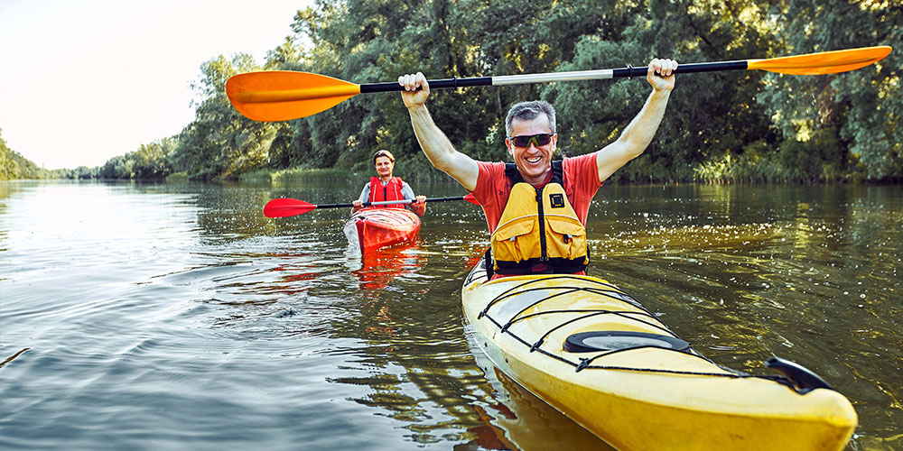 Man in a kayak facing camera holding paddle over his head